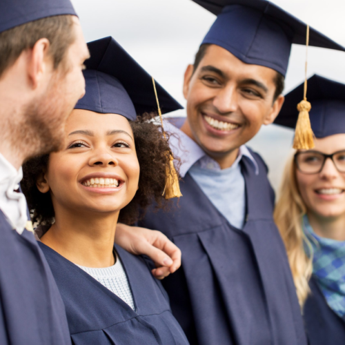 A group of young people dressed in mortar boards and graduation robes smiles at each other.